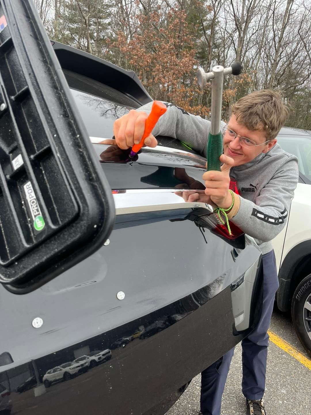 Person using tools to fix dent on black car in outdoor setting.