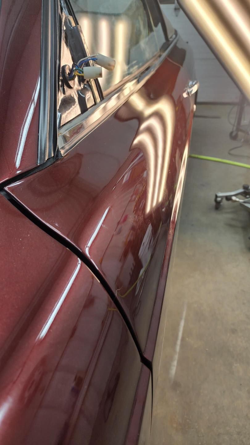 Maroon car door with several dents reflecting overhead lights.