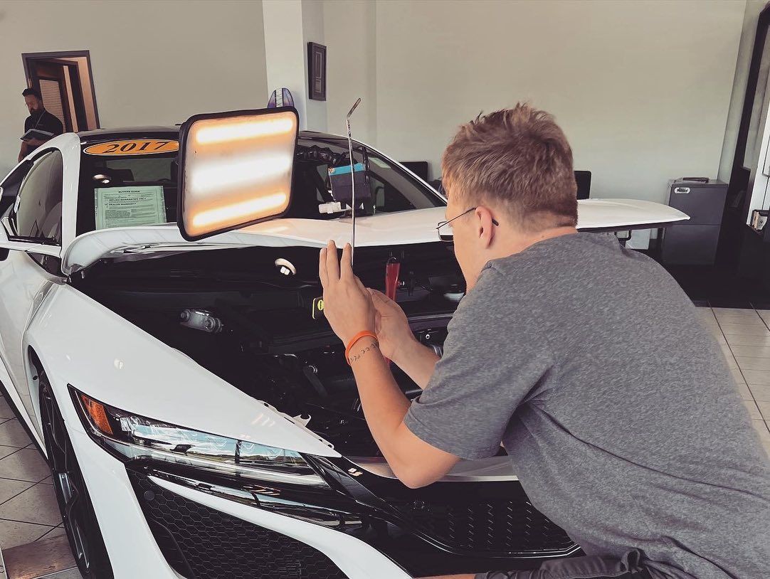 Man working on car dent in a shop, using tools. Black and white car, dent repair light.
