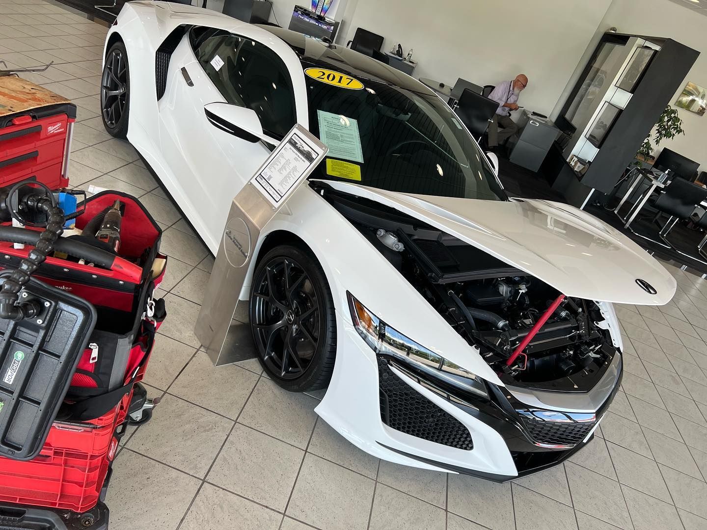 White Honda NSX sports car with the hood open, on a showroom floor.