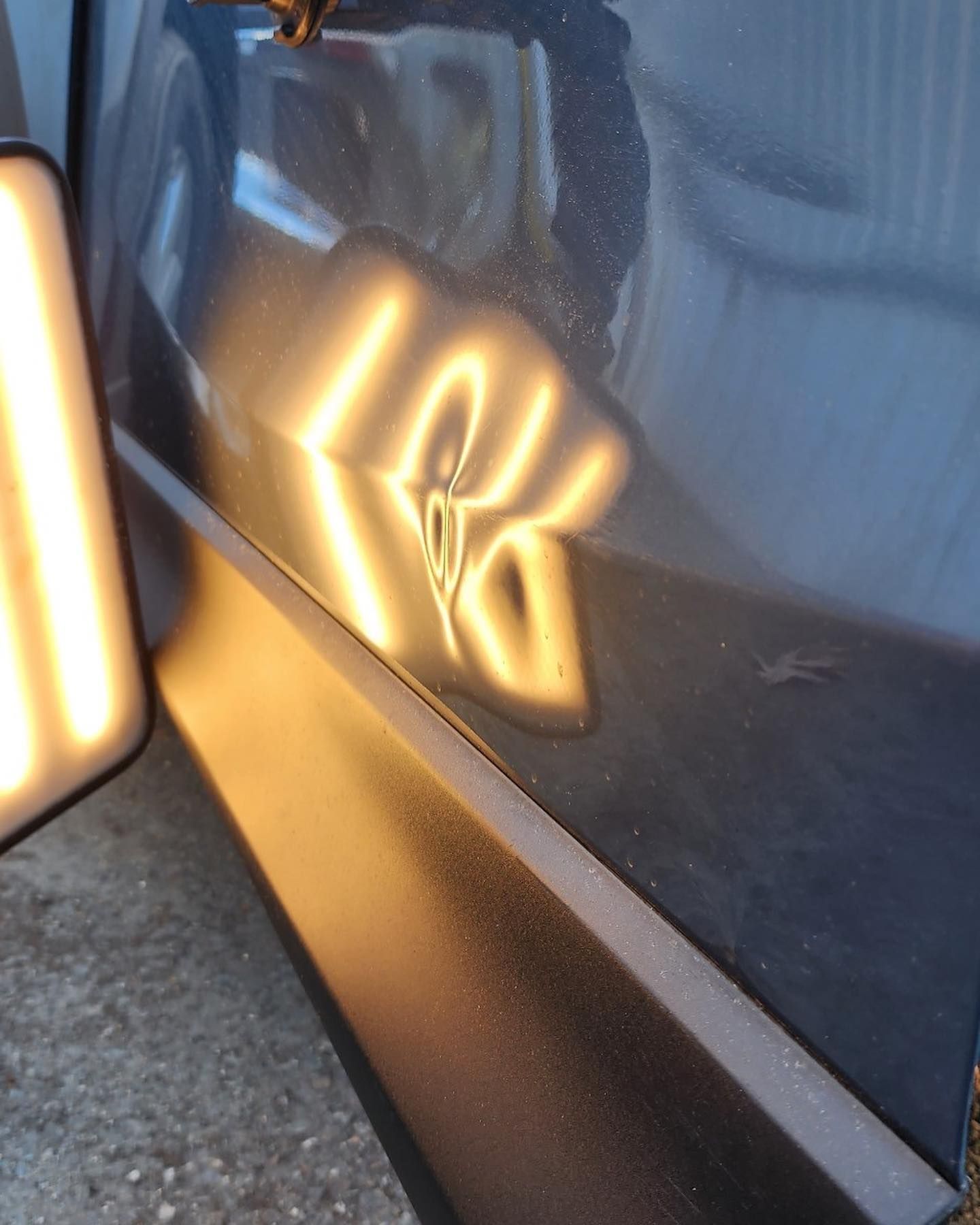 Dark gray car panel with dent; paintless dent repair in progress using a reflection board.