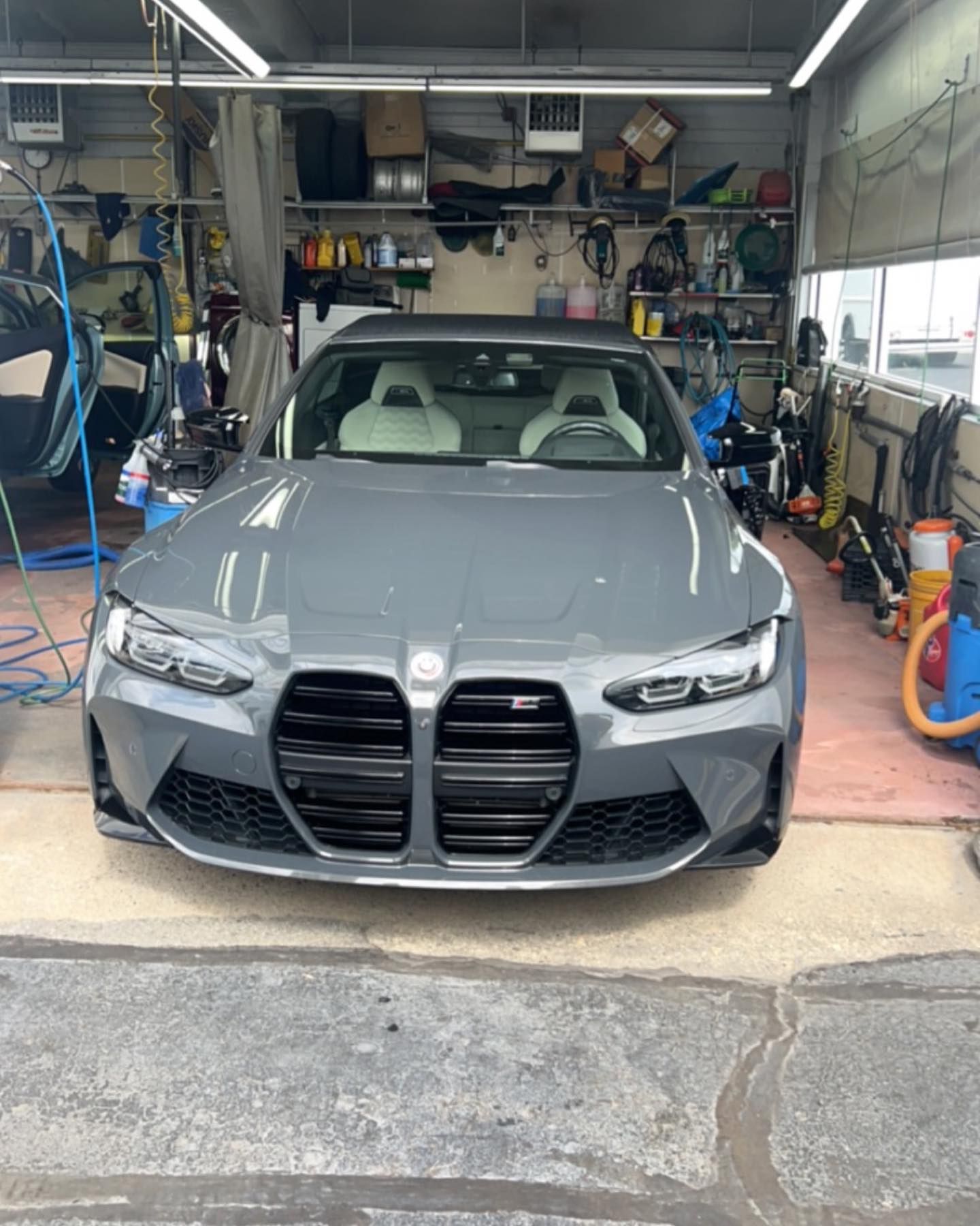 Gray BMW M4 car in a garage with white seats, black grill, and various tools.
