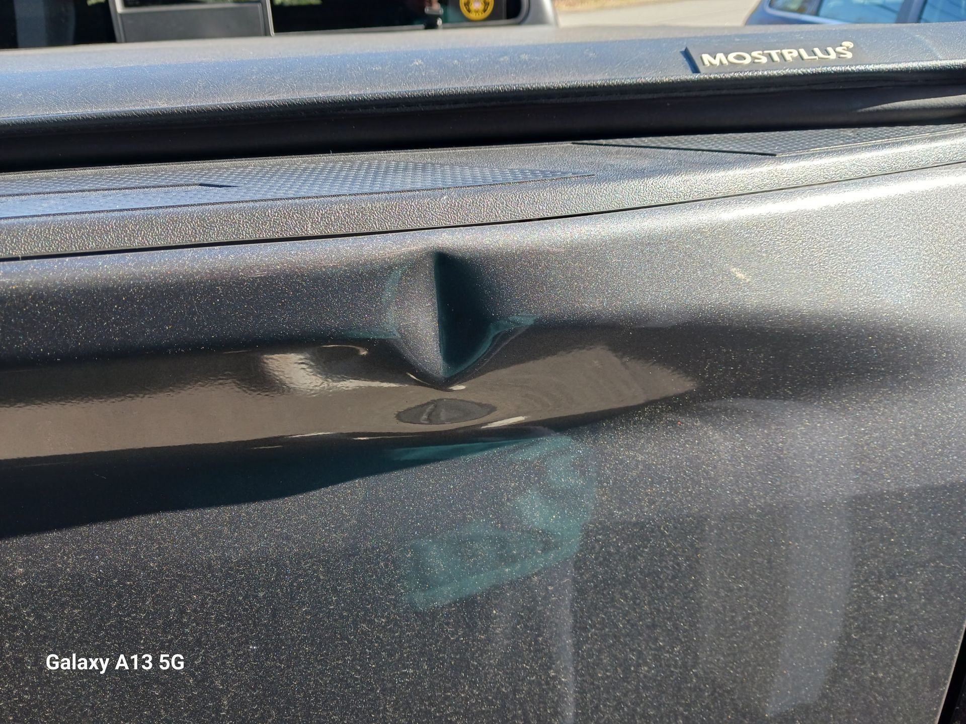 Gray truck bed with a significant dent. The bed has a bed cover.