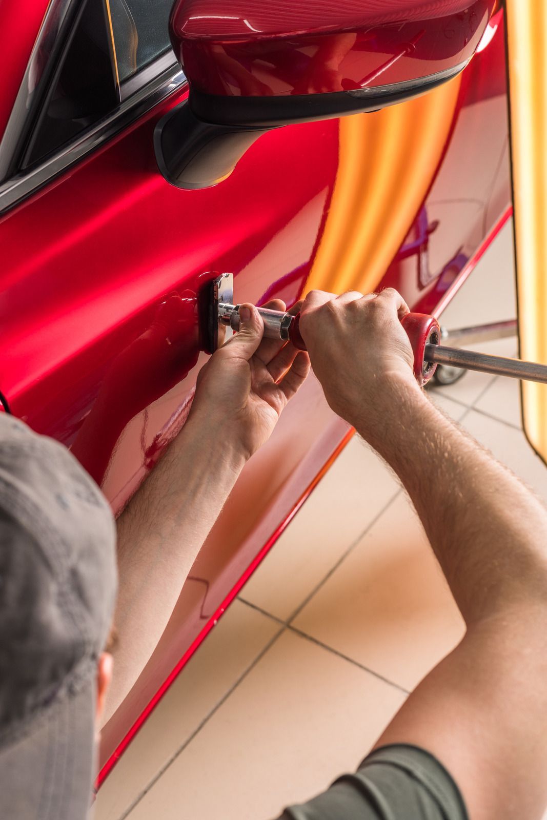 Person repairing a red car door with dent removal tools in a workshop.