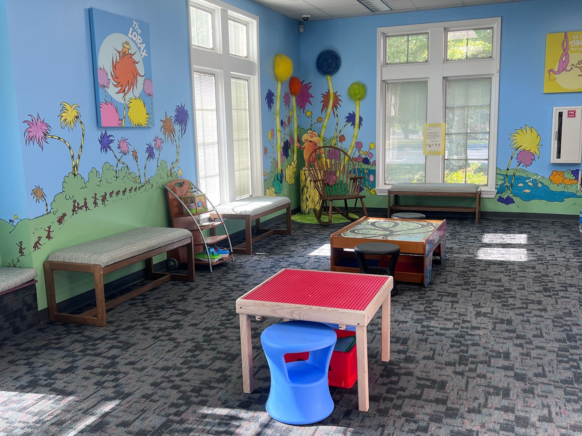 A brightly painted room with Dr. Seuss-themed murals, benches, tables, and windows.