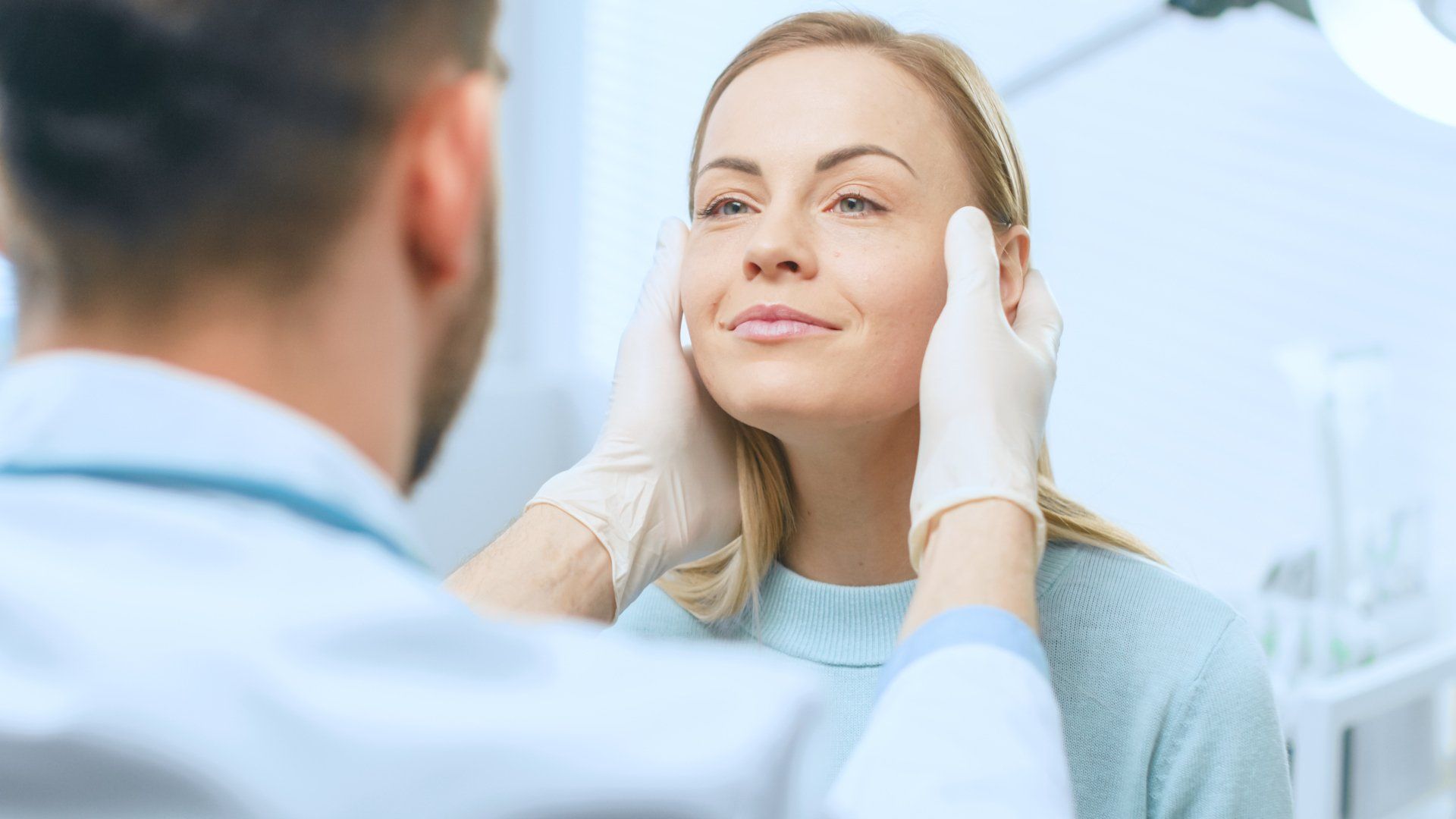 Doctor examining a woman's face, checking for wrinkles. Medical setting with overhead lights.