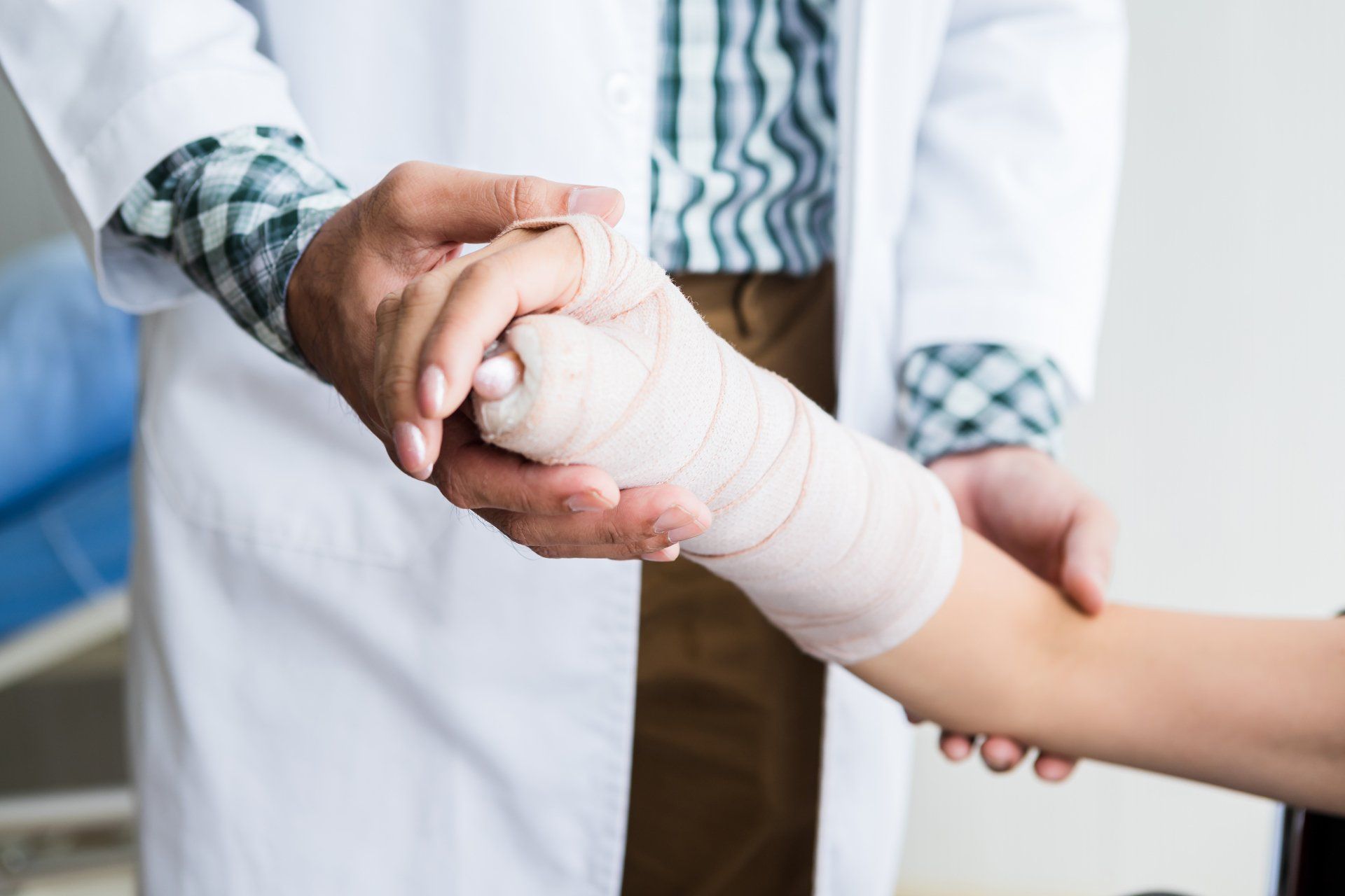 Doctor examining a patient's bandaged wrist and hand, indoors.