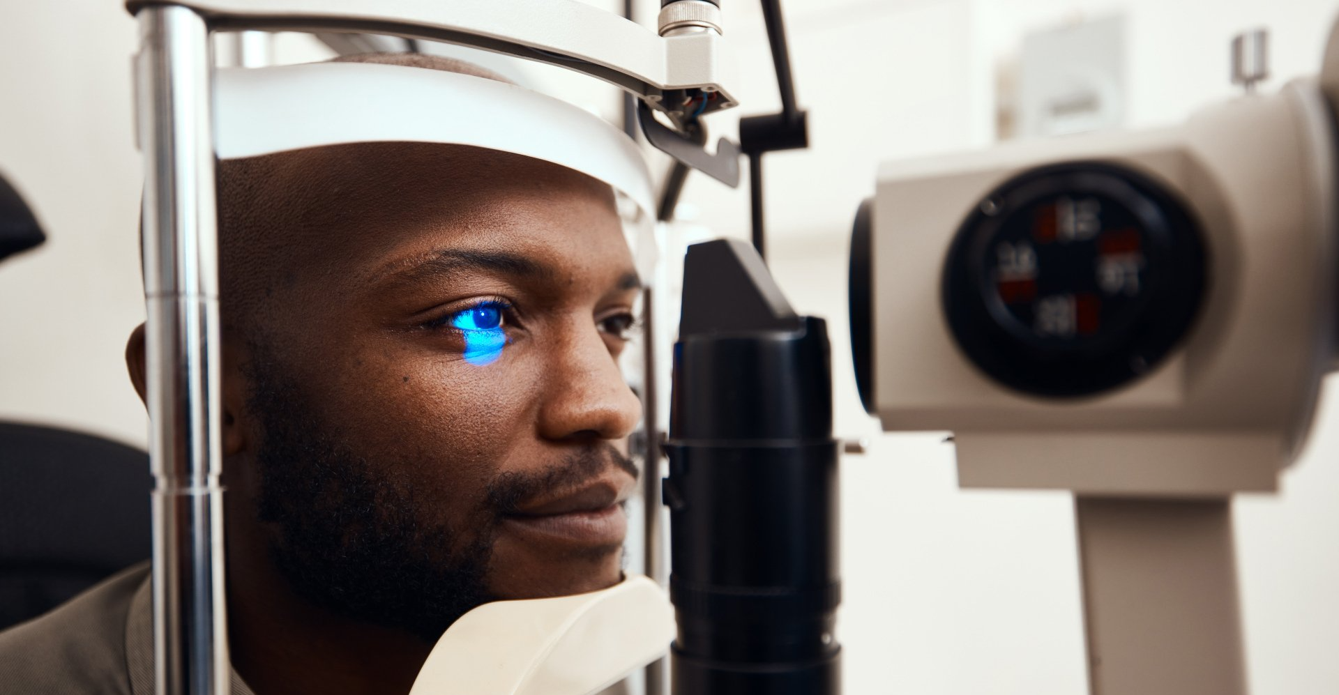 Man undergoing an eye exam with a blue light shining on his eye in a clinical setting.