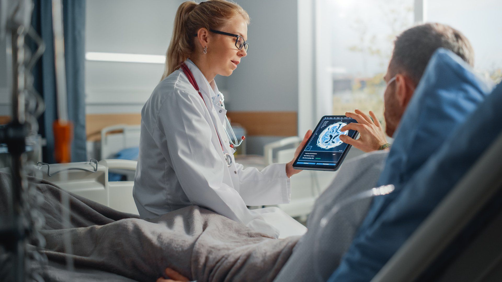 Doctor showing patient a tablet with medical scan, hospital bed.