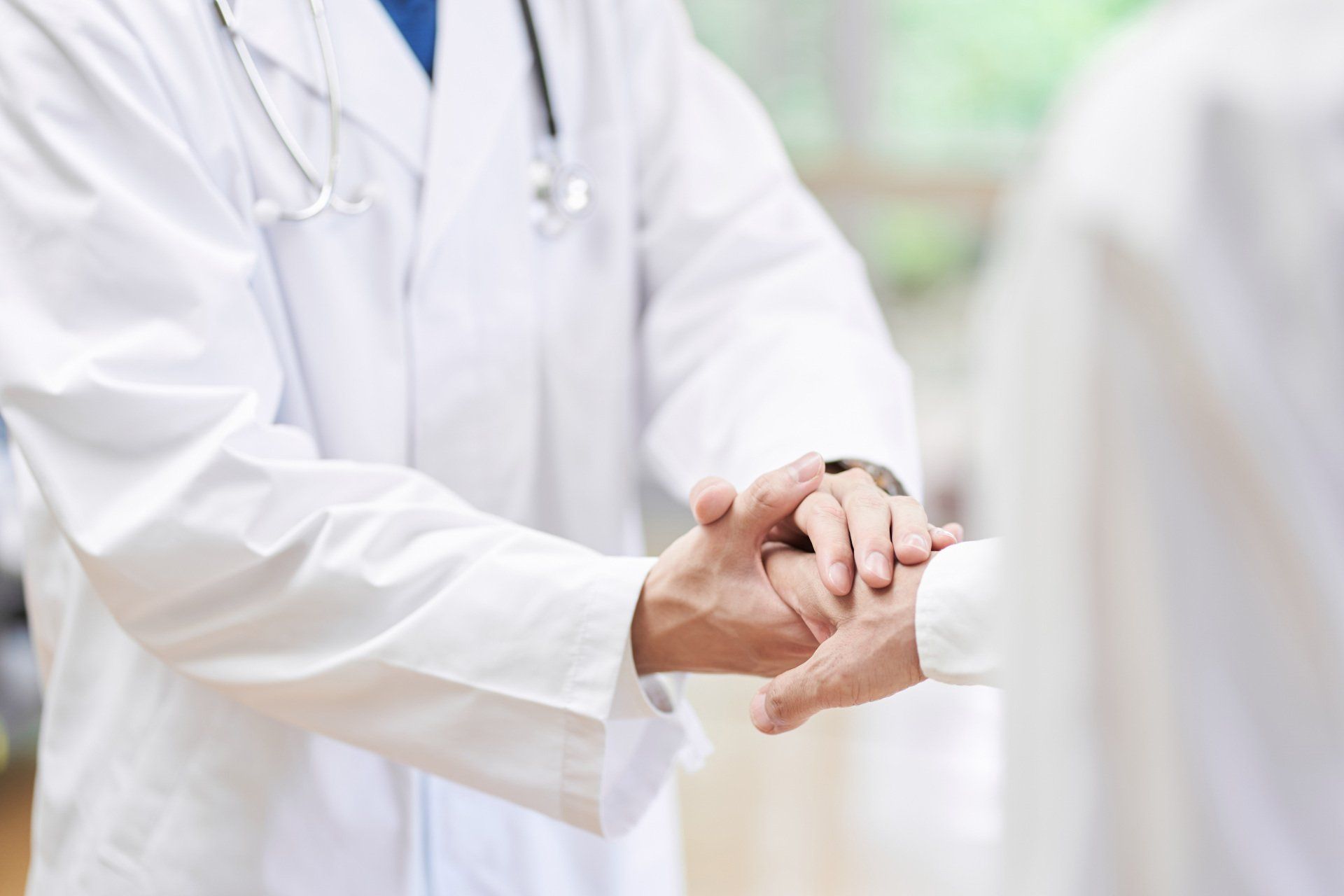 Doctor in white coat holds patient's hand, offering comfort and support.