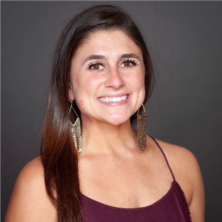 Smiling woman with dark hair and gold earrings in front of a gray backdrop.