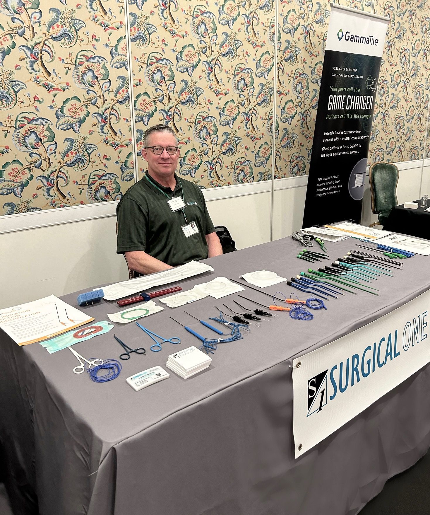 Man at surgical tools display booth. Tools laid out on table. Black and white banner visible.