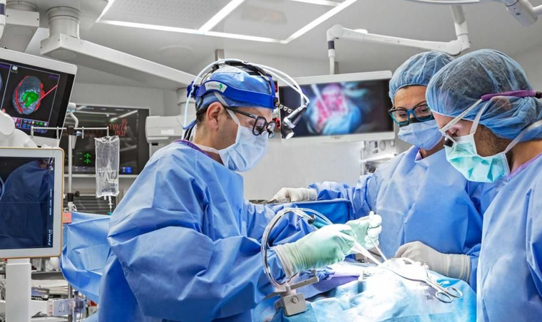Surgeons in blue scrubs operating in a bright operating room.