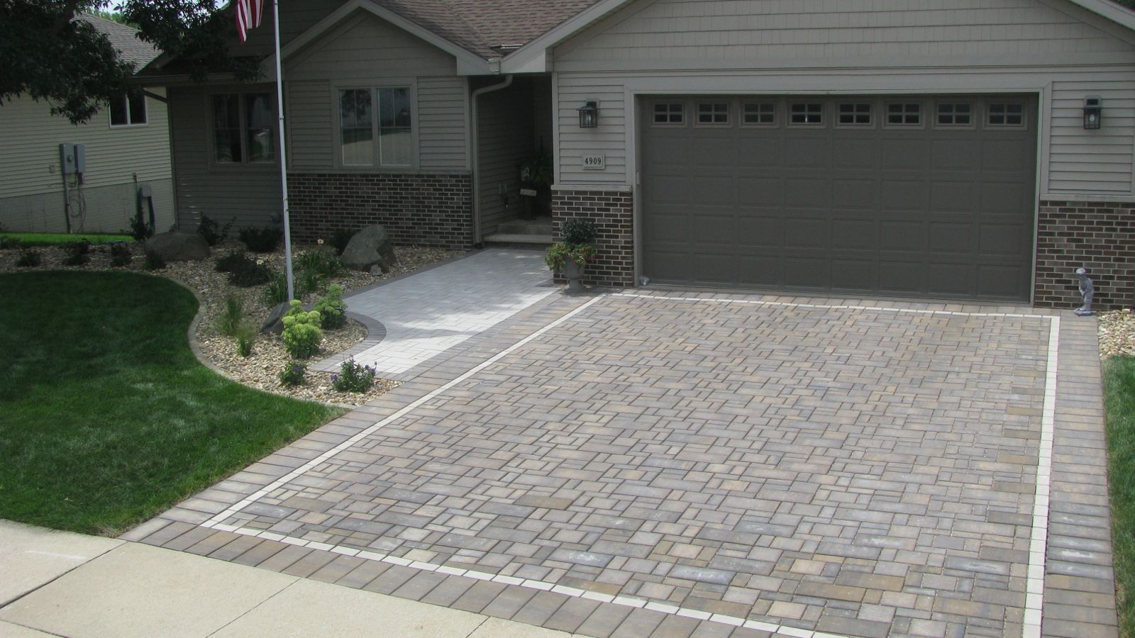 House with brick driveway and sidewalk leading to the front door. Brown garage door and beige siding.