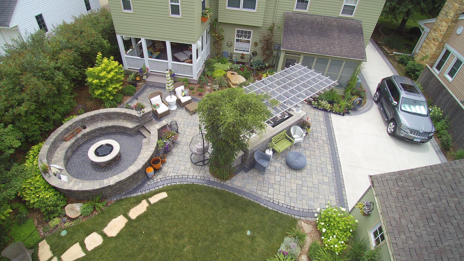 Aerial view of a backyard with a circular fire pit, patio, gazebo, and parked car.