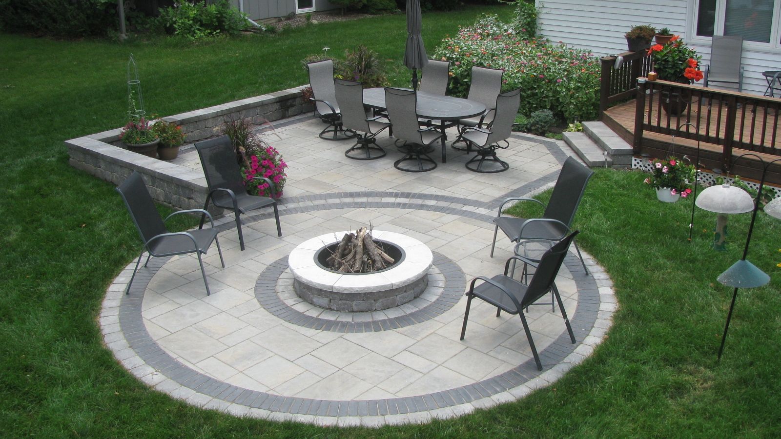 Outdoor patio with fire pit, seating, and a dining area, set on a green lawn.