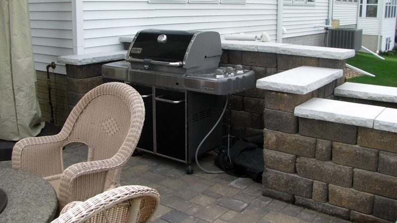 Outdoor grilling area with a grill, stone wall, chairs, and patio.