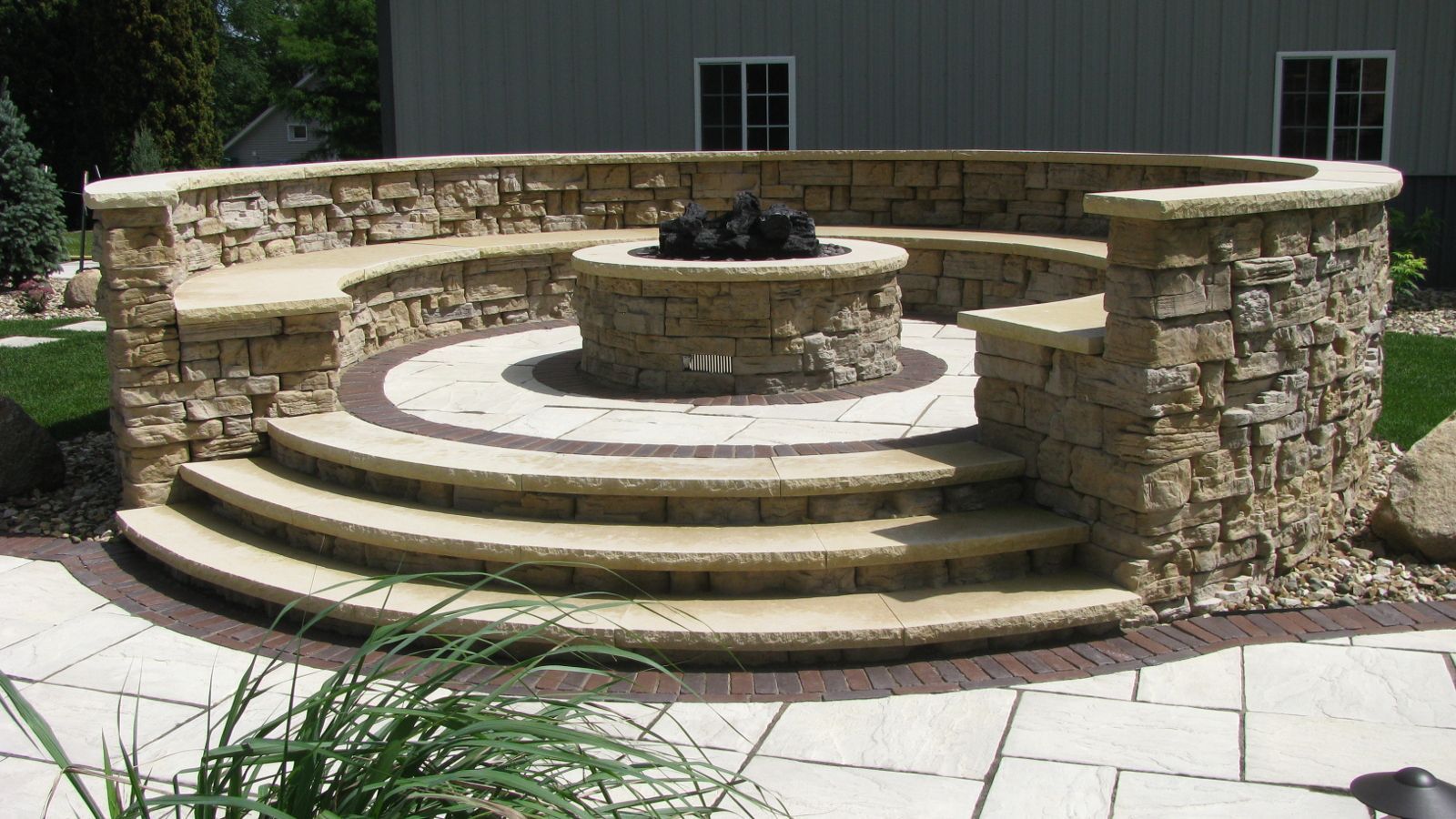 Circular stone fire pit and seating area in a backyard.
