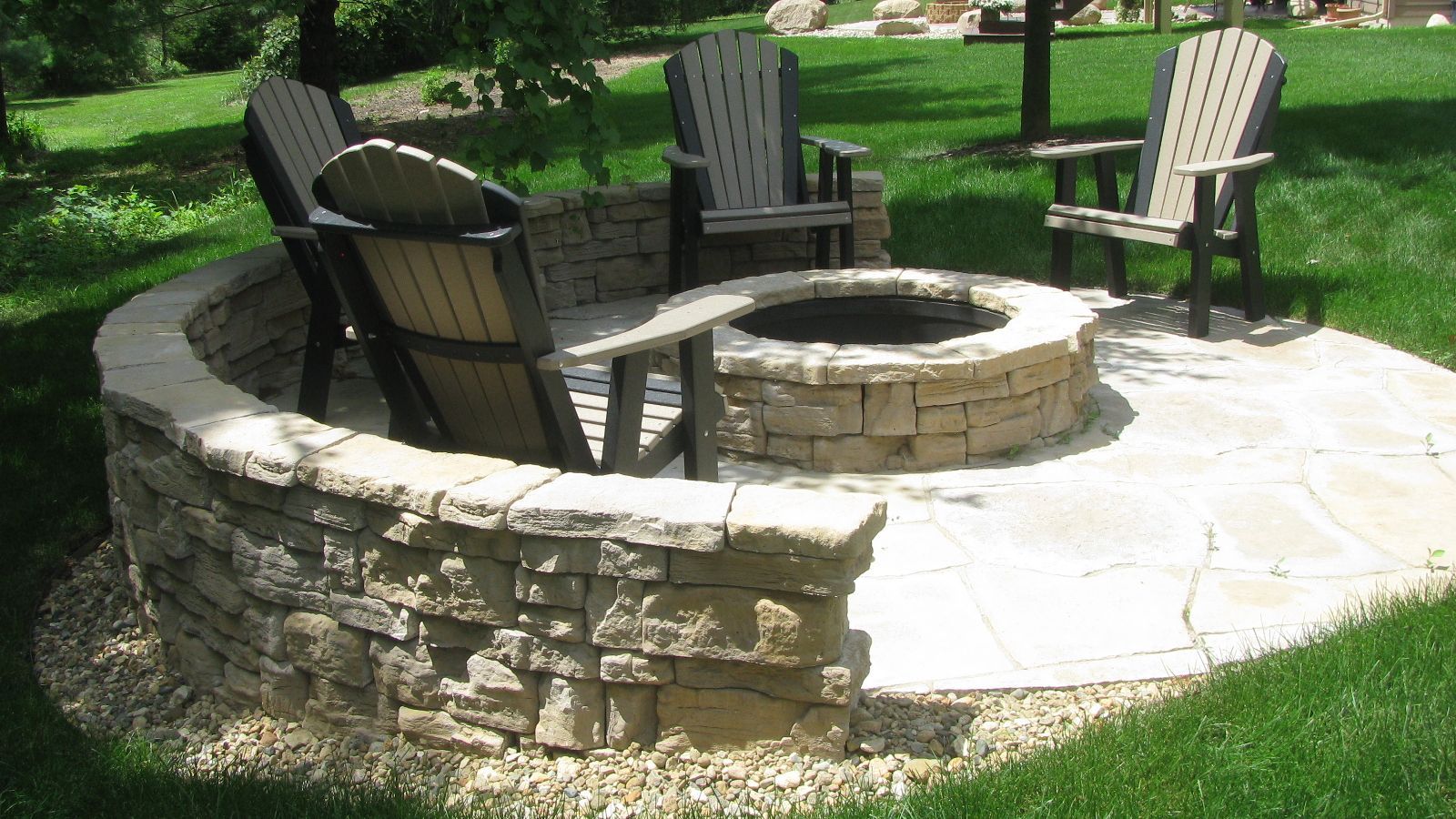 Stone fire pit with surrounding seating area and Adirondack chairs.