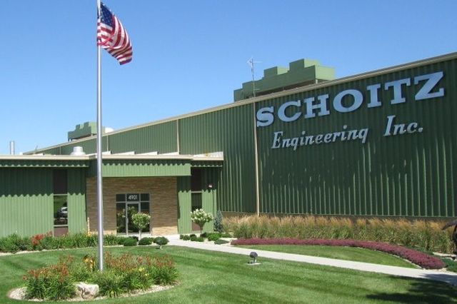 Exterior of Schotiz Engineering Inc. building with American flag, green facade, and manicured lawn.