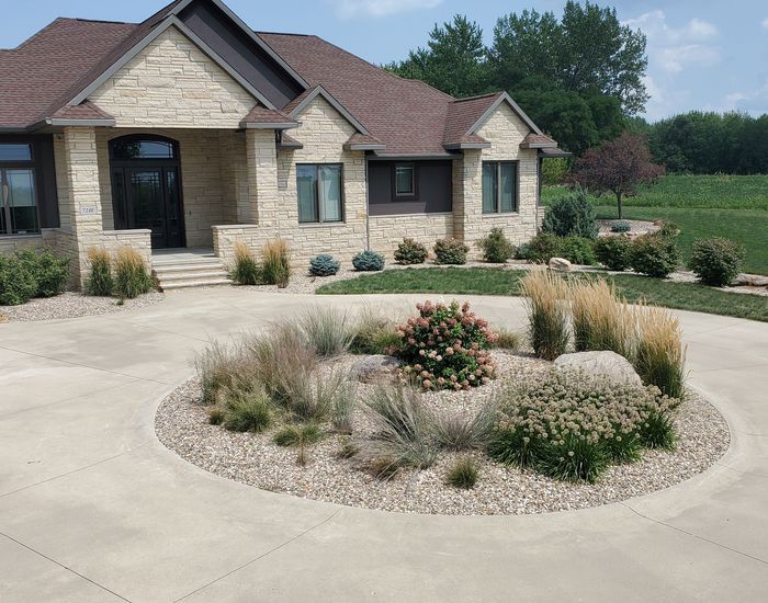 Stone house with circular driveway and rock garden.