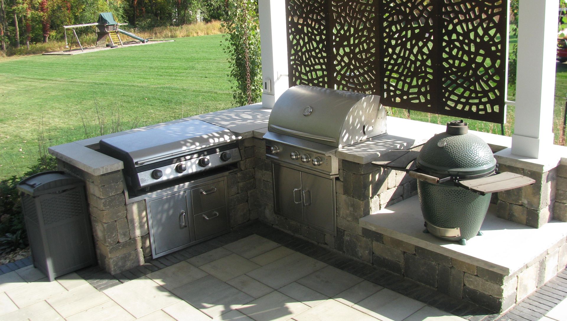 Outdoor grilling station with built-in gas grill, Big Green Egg, and decorative screen.