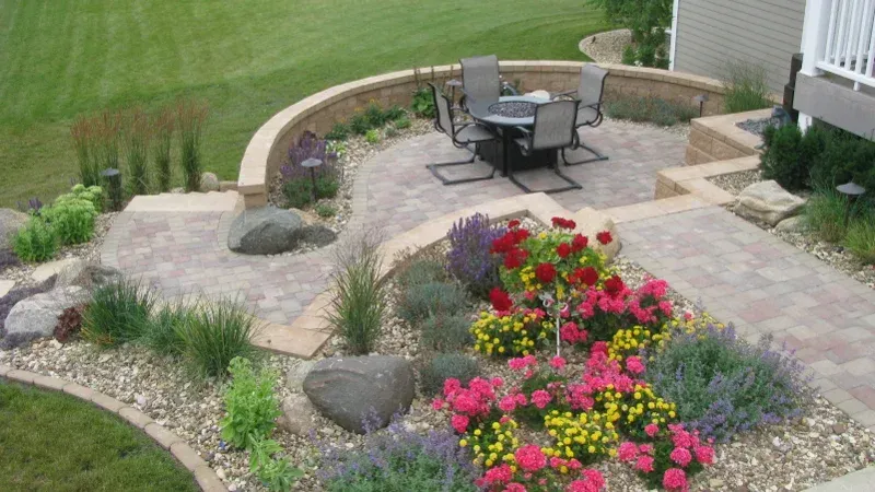 A patio with a table and chairs surrounded by flowers and rocks — Waterloo, IA — Matthias Landscaping Co