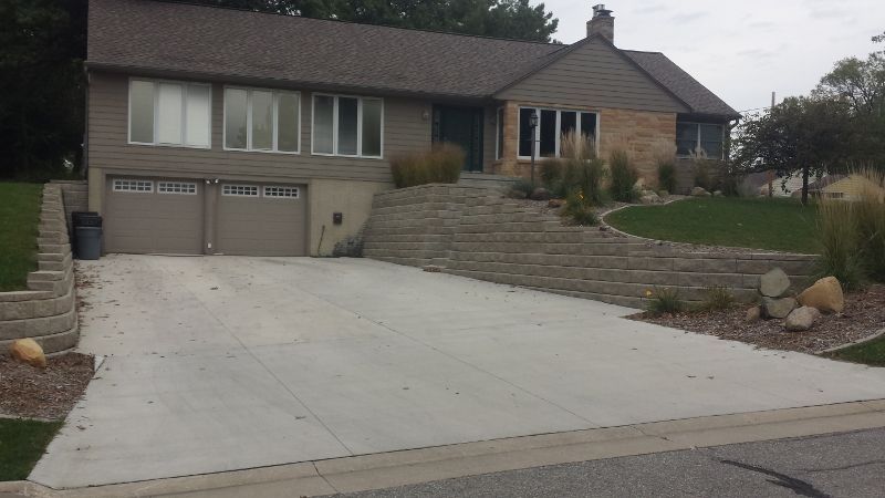 A two-story house with a sloped yard, stone retaining walls, driveway, and garage.