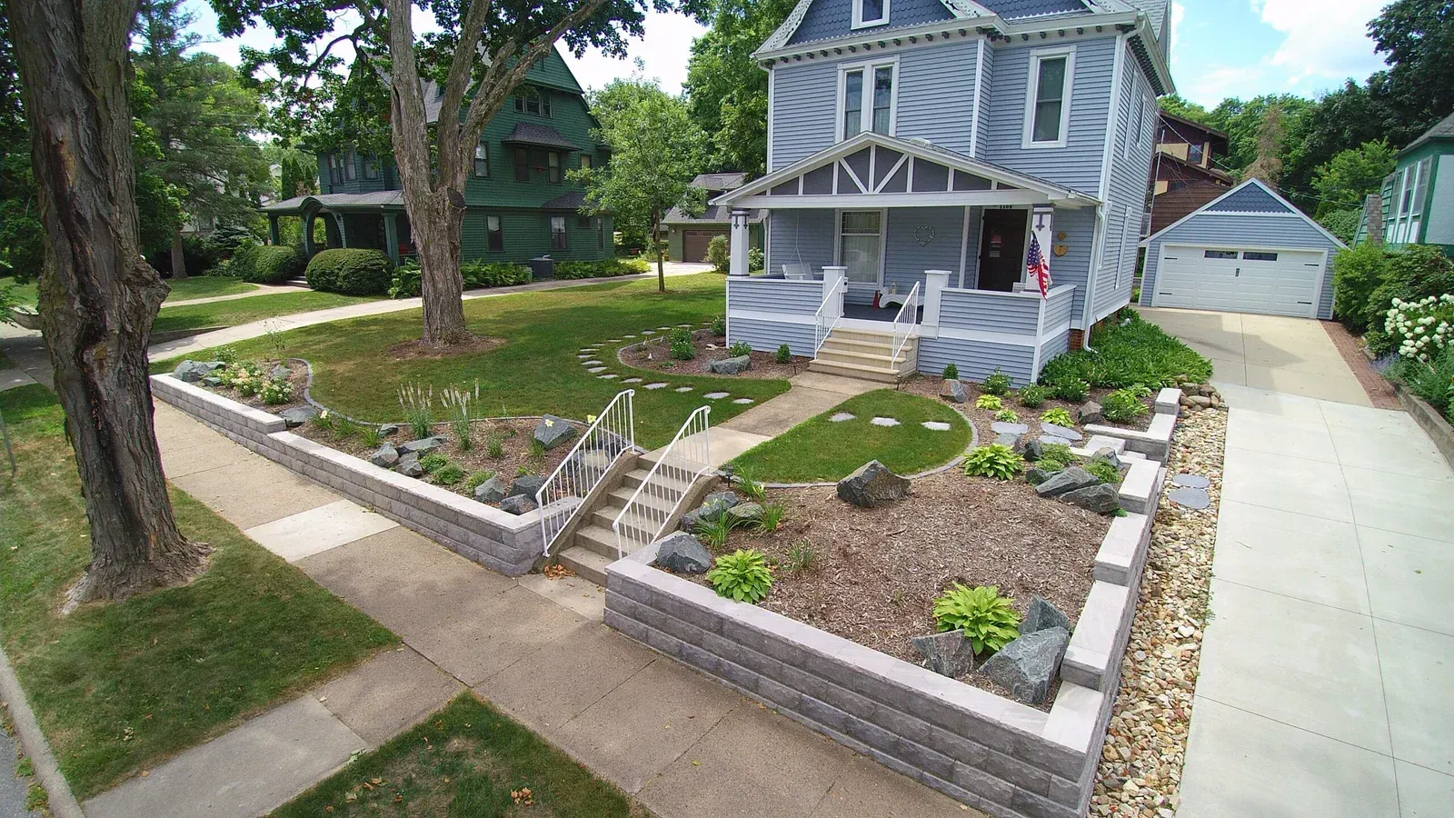 An aerial view of a house with a lush green lawn and a stone wall in front of it — Waterloo, IA — Matthias Landscaping Co