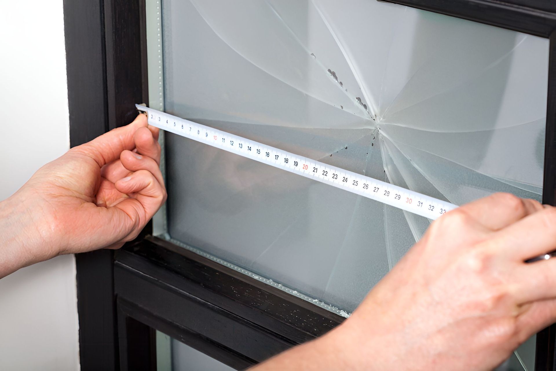 A Person is Measuring a Broken Window With a Tape Measure — Twin Cities Glass In Albury, NSW