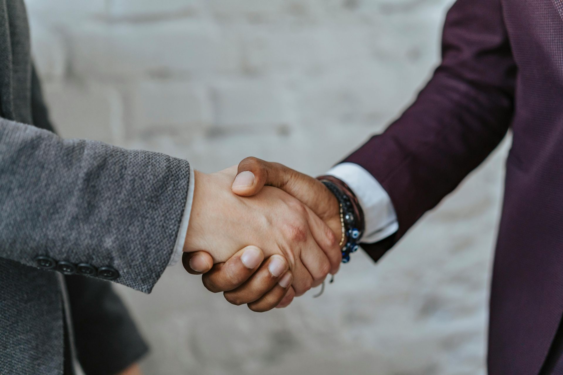 Two men are shaking hands in front of a brick wall.