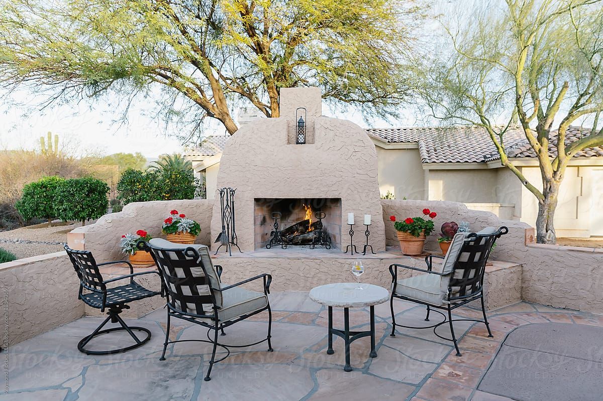 A patio with a fireplace and chairs in front of it.