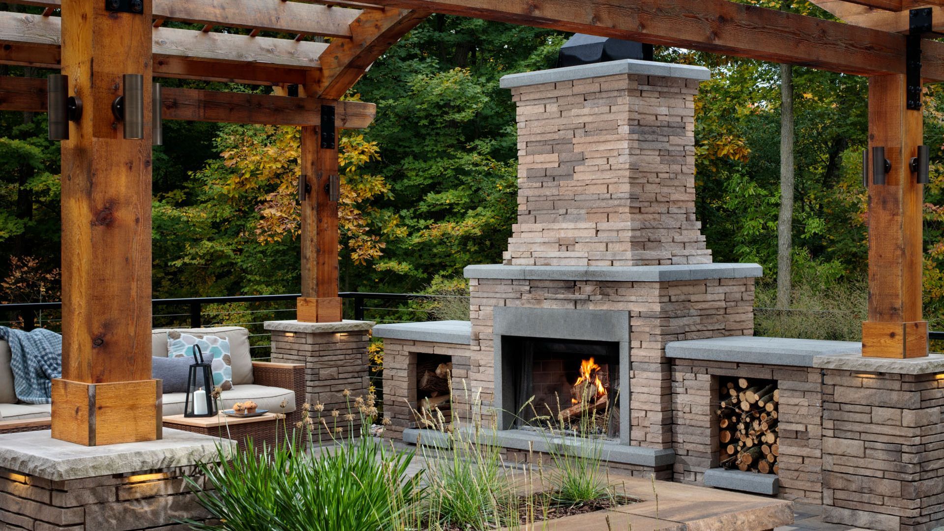 A brick fireplace is sitting under a wooden pergola in a backyard.