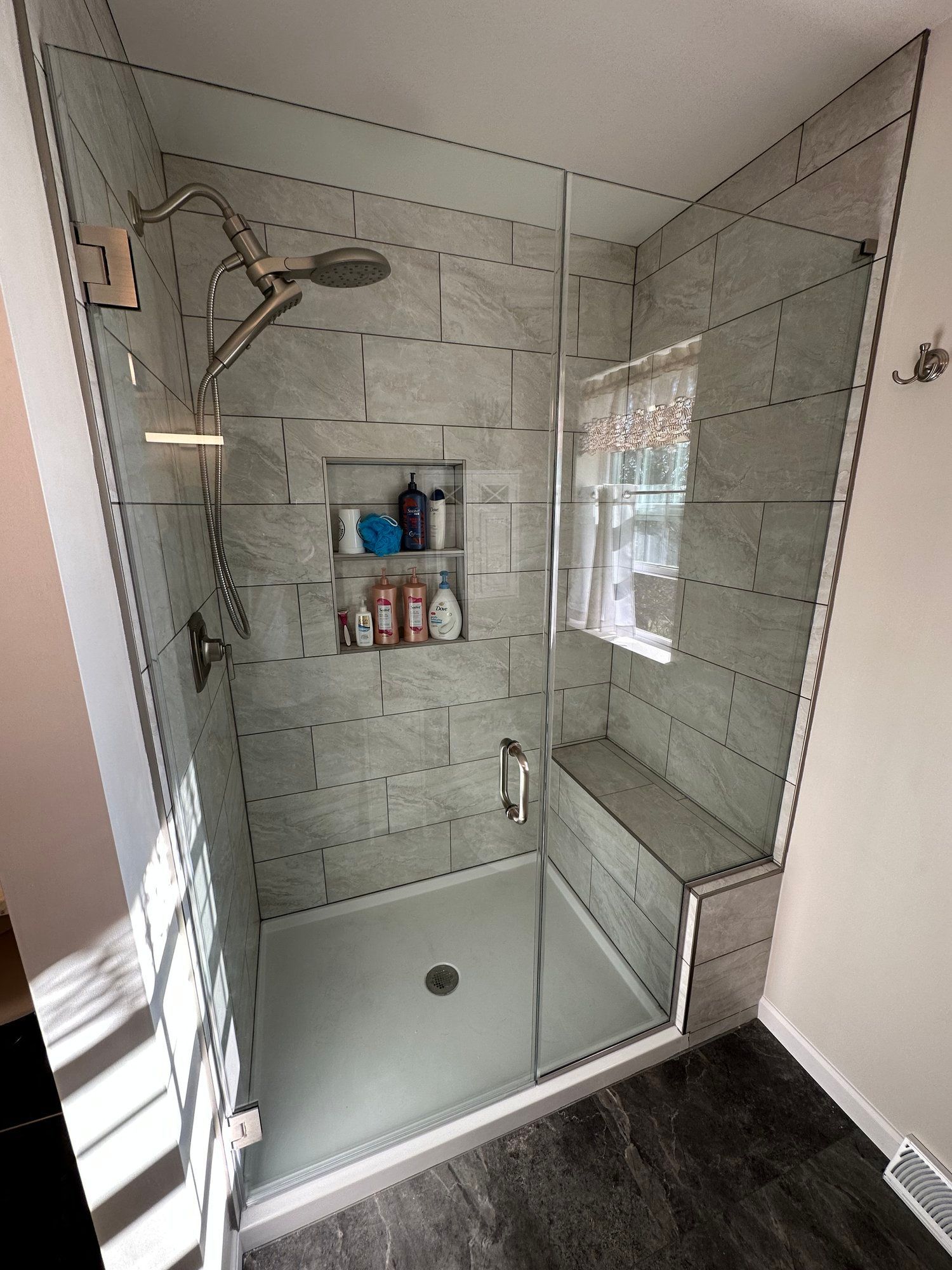 A bathroom with a walk in shower with a glass door and a window.