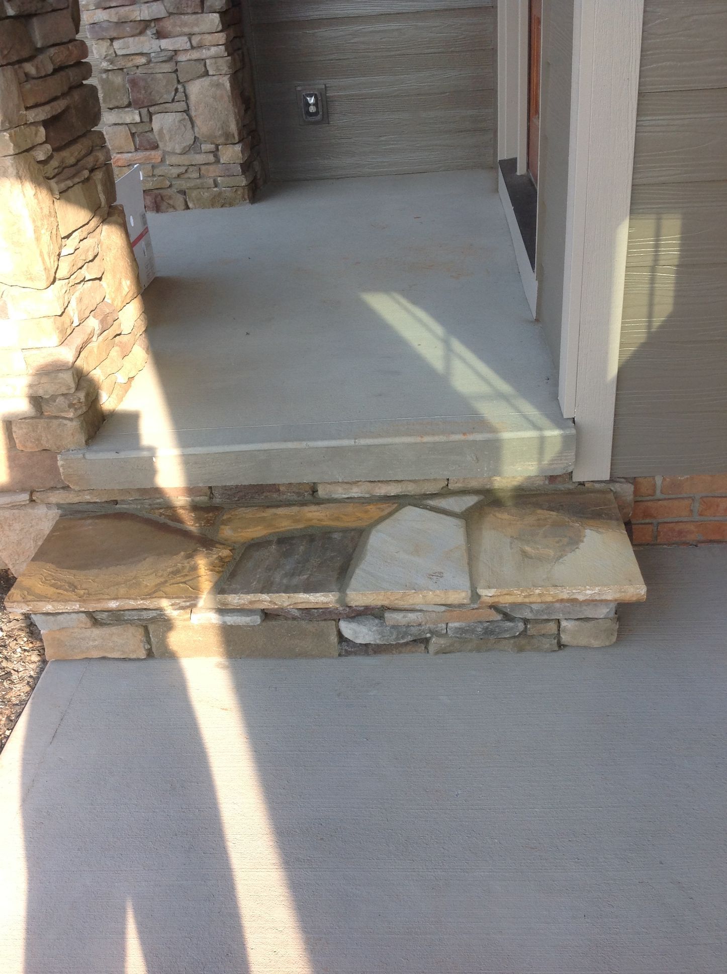 A concrete porch with stone steps and a stone wall.