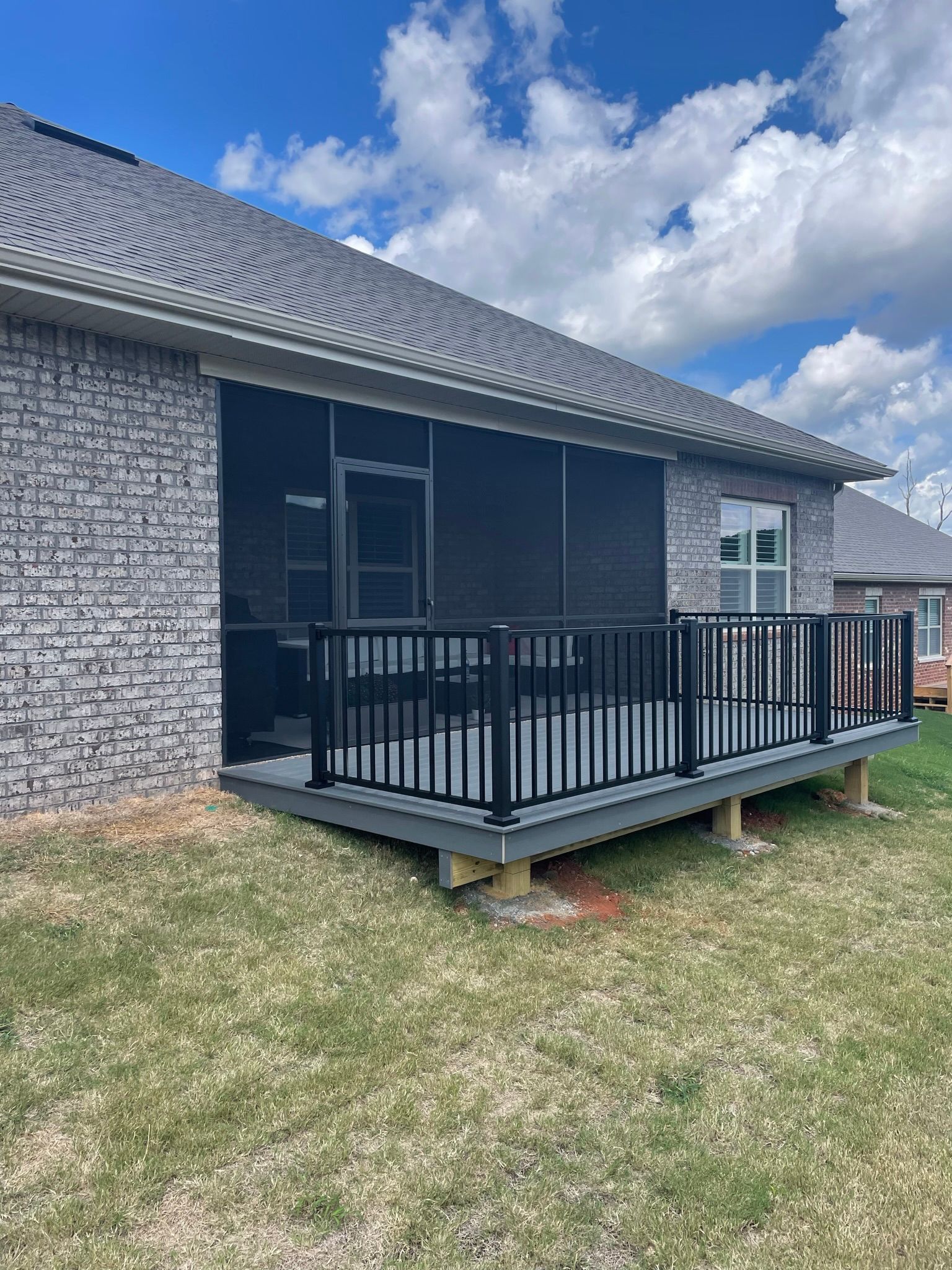 A screened in porch is sitting in front of a brick house.