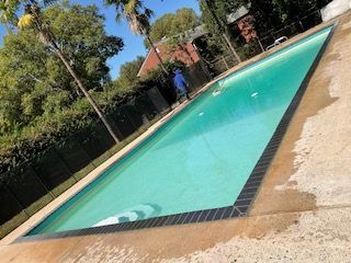 A large swimming pool is surrounded by trees and a fence.