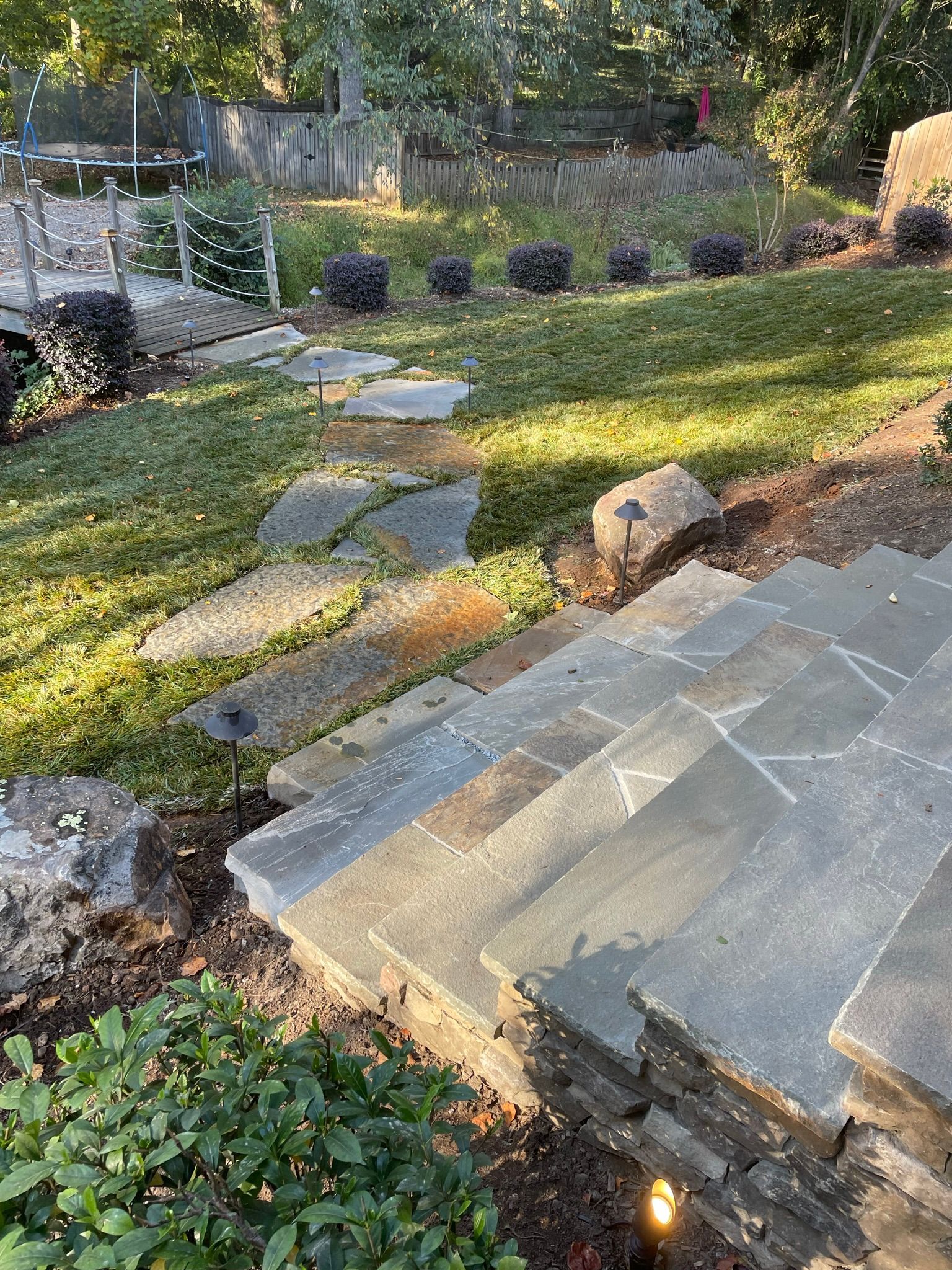 A stone walkway leading to a patio in a backyard.