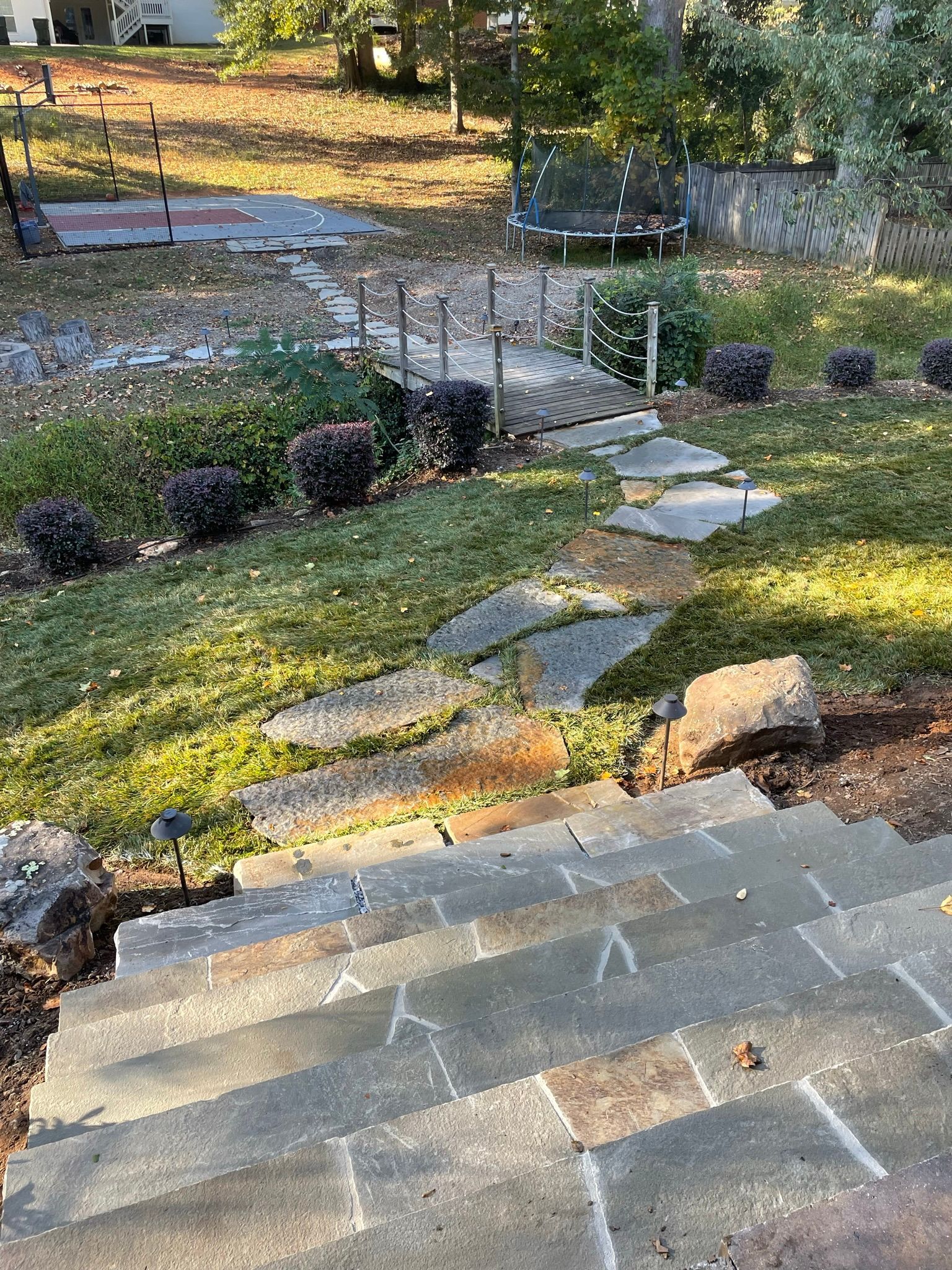 A stone walkway leading to a trampoline in a backyard.