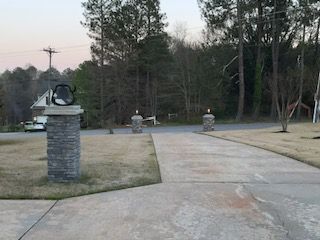 A concrete driveway leading to a house with trees in the background.