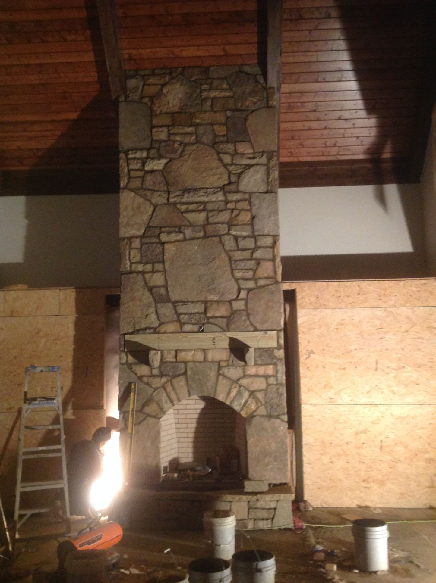 A stone fireplace is being built in a room with a wooden ceiling.
