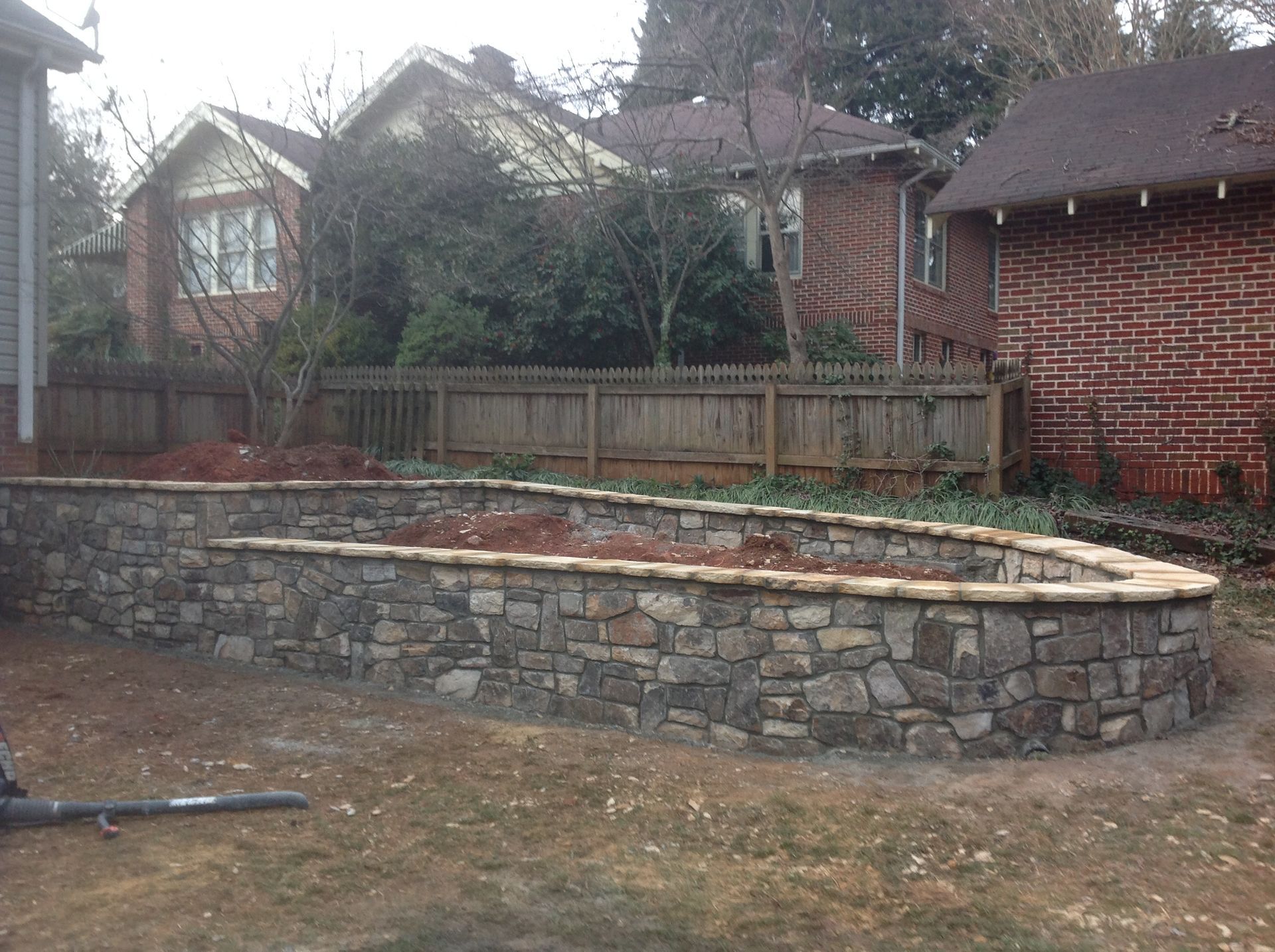 A stone wall is being built in the backyard of a house.
