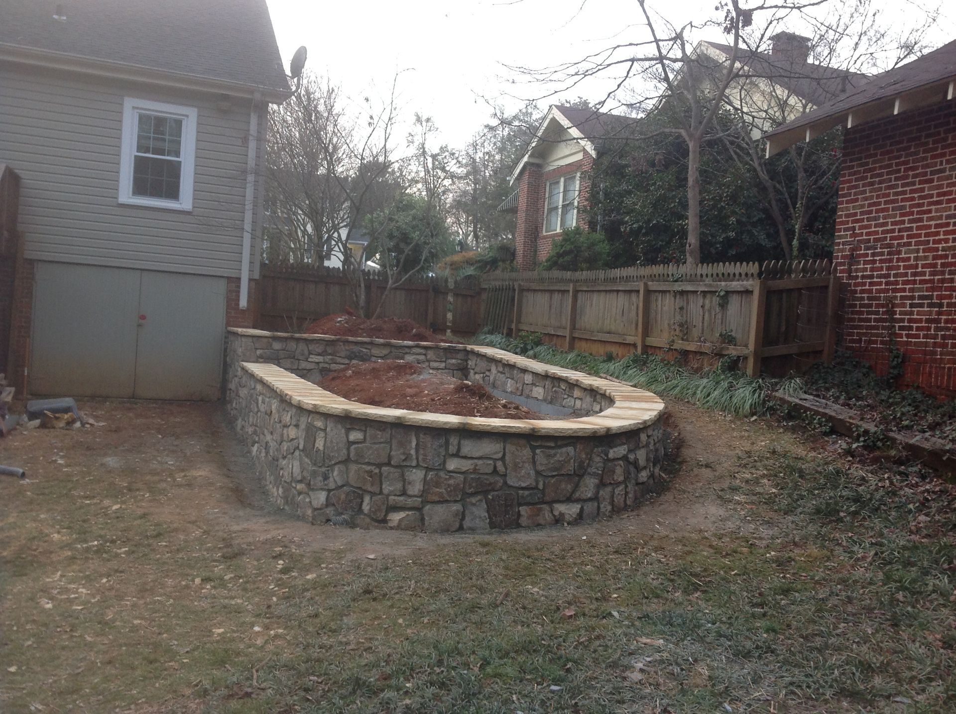 A stone wall is being built in the backyard of a house
