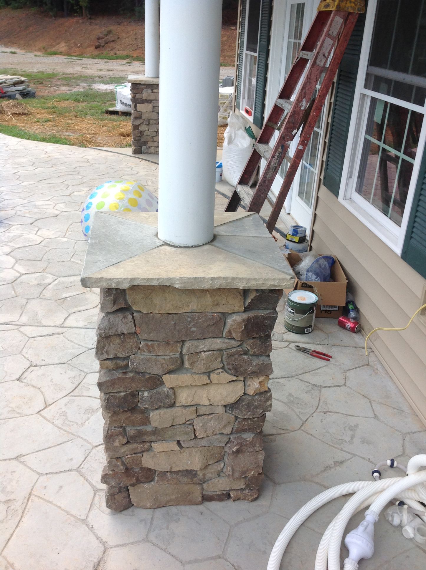 A ladder is sitting on a porch next to a stone column.