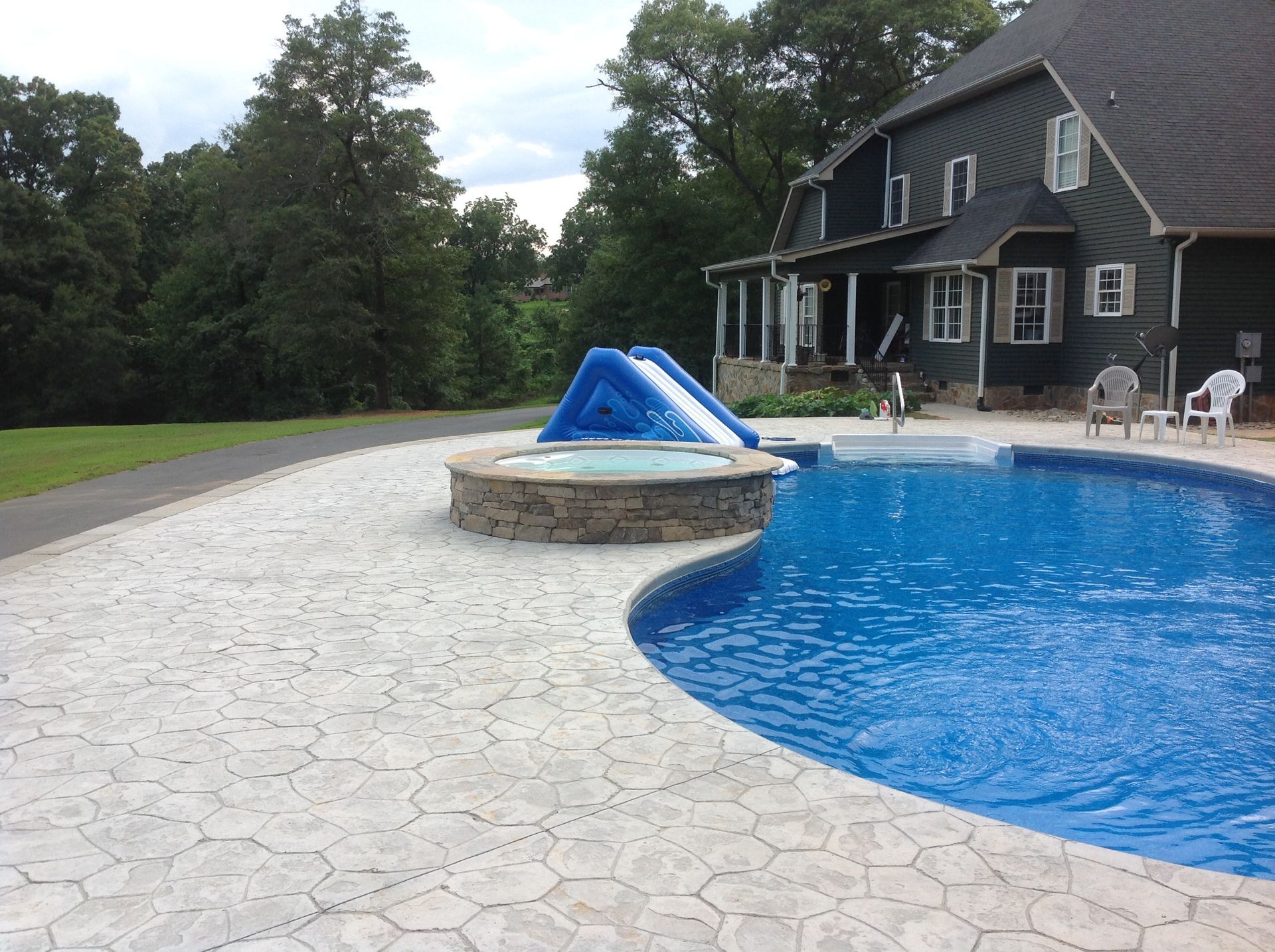 A large swimming pool is surrounded by a patio and a house