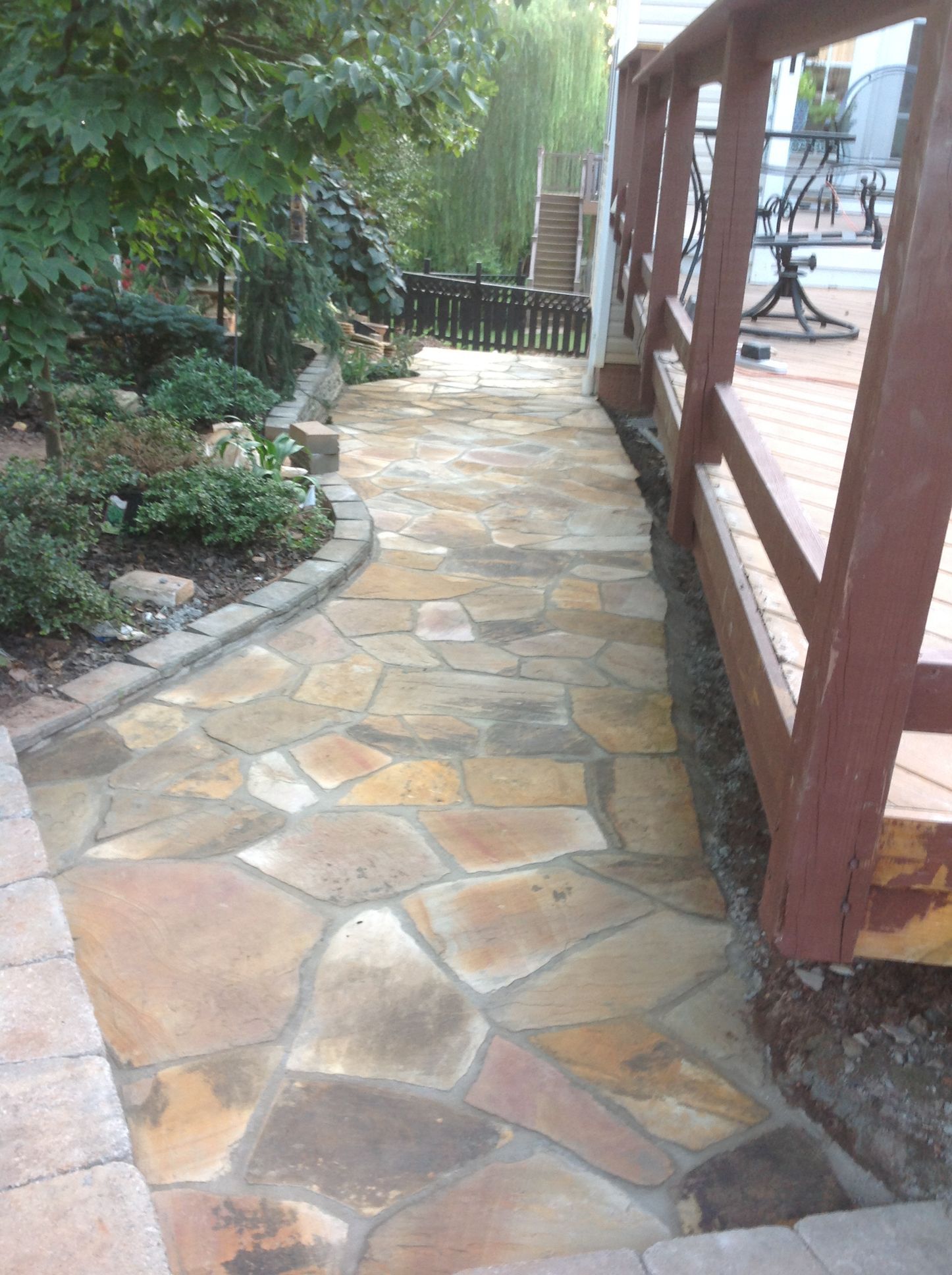 A stone walkway leading to a wooden deck in a backyard.
