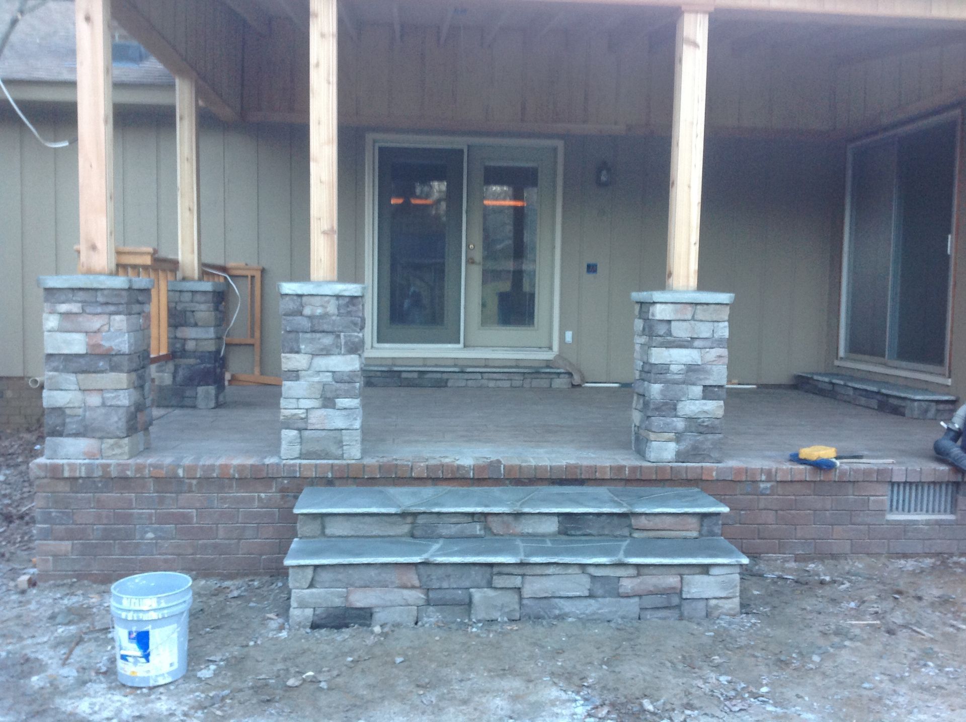 A brick porch with steps and a blue bucket in front of it