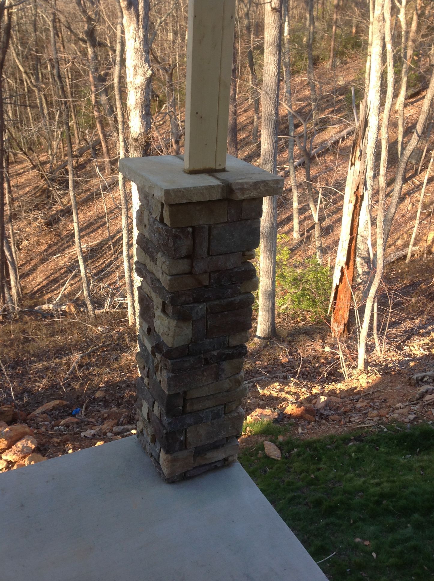 A stone column is sitting on a porch with trees in the background.