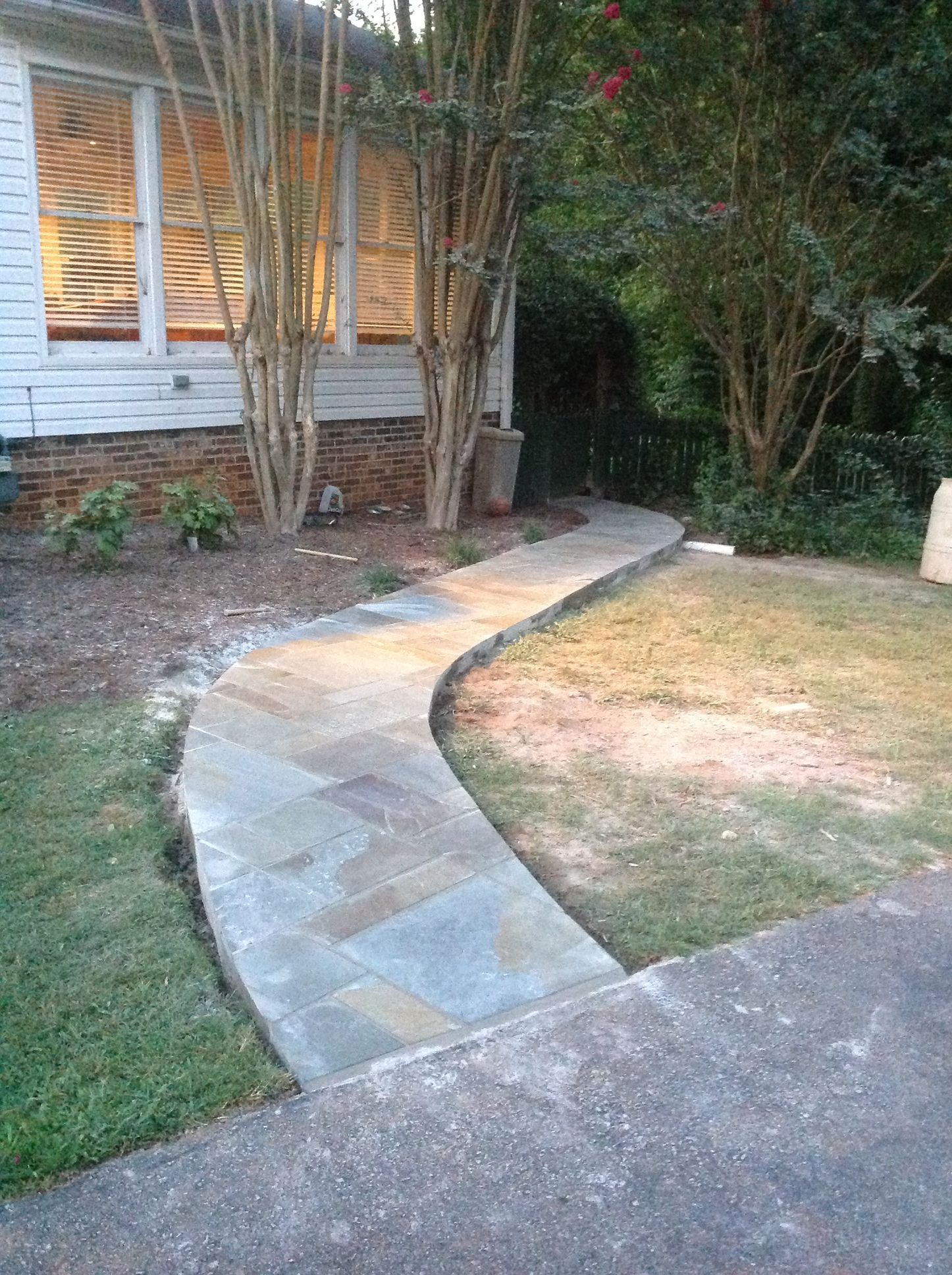 A stone walkway leading to a house with trees in the background.
