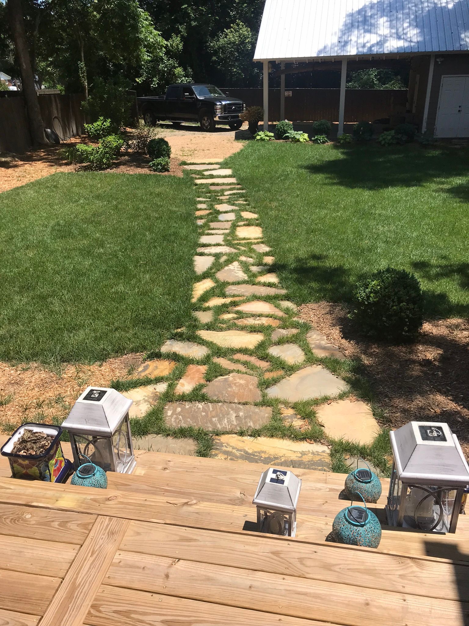 A wooden deck with a stone walkway leading to a house.